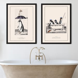 Op de afbeelding: Twee ingelijste kunstprints met pingu&iuml;n illustraties. E&eacute;n toont een pingu&iuml;n in de douche met een paraplu, de andere toont pingu&iuml;ns in een badkuip die aan het vissen zijn. Beide prints hebben zwarte lijsten en tekst onderaan.