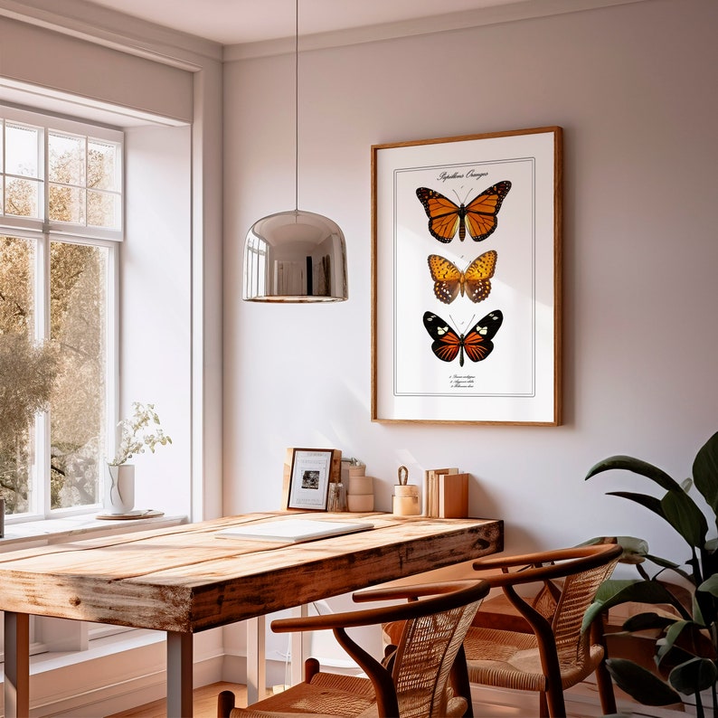 May include: A framed print of three butterflies with orange and black wings. The print is hanging on a white wall above a wooden table with two chairs.