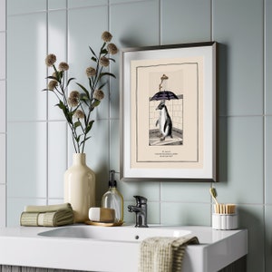 Op de afbeelding: Ingelijste kunstdruk met een pingu&iuml;n onder een paraplu in een douche, met tekst eronder. De print zit in een zilveren lijst, tentoongesteld op een wit aanrecht met een vaas met bloemen, een zeepdispenser en handdoeken. De achtergrond is een lichtblauwe tegelmuur.