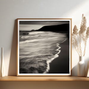 May include: A black and white photograph of a beach scene with waves crashing on the shore. The photo is framed in a wooden frame.