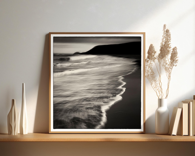 May include: A black and white photograph of a beach scene with waves crashing on the shore. The photo is framed in a wooden frame.
