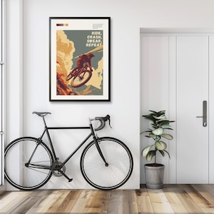 May include: A framed poster with the text "RIDE, CRASH, SWEAR, REPEAT" and an illustration of a mountain biker. A black road bike is leaning against the wall. A potted plant sits next to a white door.