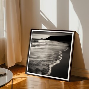May include: Black and white photograph of a beach scene with waves crashing on the shore. The photo is framed in a black frame.
