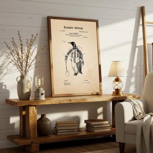 May include: A framed vintage patent print featuring a penguin in a suit holding a shovel. The print is in sepia tones with the text "Patent Office" at the top. The print is displayed on a rustic wooden console table with decorative items.