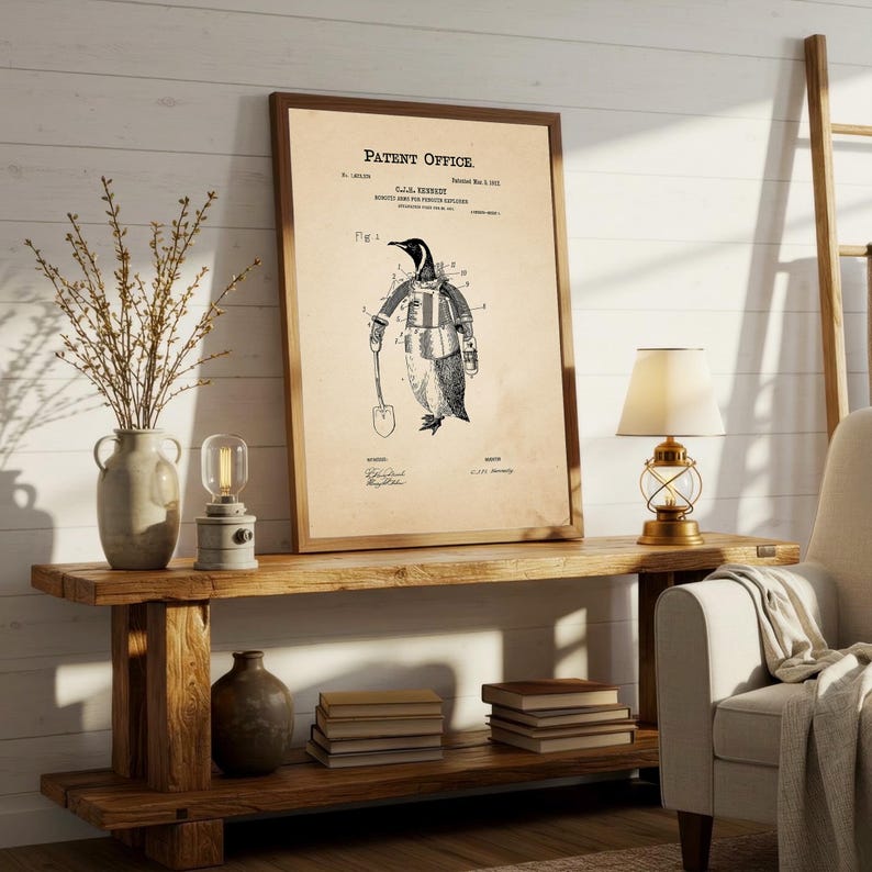 May include: A framed vintage patent print featuring a penguin in a suit holding a shovel. The print is in sepia tones with the text "Patent Office" at the top. The print is displayed on a rustic wooden console table with decorative items.
