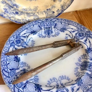 May include: A vintage metal nutcracker with a textured surface, resting on a blue and white porcelain plate with a floral pattern.