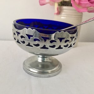 May include: A cobalt blue glass sugar bowl with a silver, openwork rim and a silver base.