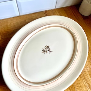 May include: A white oval ceramic serving platter with a brown rim and a simple brown floral design in the center.