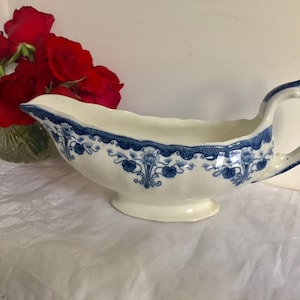 May include: A white porcelain gravy boat with a blue and white floral design. The boat has a handle and a spout.