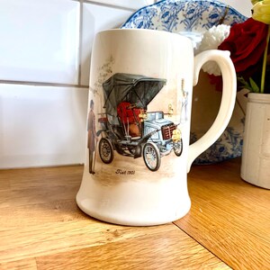 Peut inclure: Une tasse en céramique blanche avec une anse présente une illustration vintage d'une Fiat bleue de 1901. La voiture est représentée avec un intérieur rouge et un conducteur en costume marron. La tasse porte l'inscription "Fiat 1901" imprimée au fond.