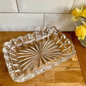 Puede incluir: Un plato de vidrio transparente con un diseño de vidrio cortado. El plato es rectangular con bordes redondeados y tiene un patrón de estrella en el centro.