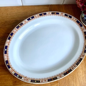 May include: A white oval serving platter with a blue and gold decorative border. The border features a repeating pattern of stylised flowers and leaves.