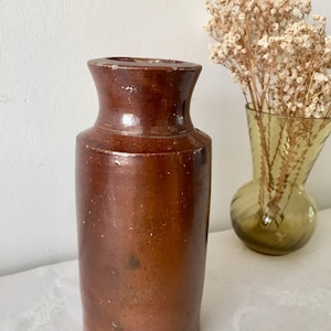 Może przedstawiać: Brązowy ceramiczny wazon z szeroką szyjką i zaokrąglonym korpusem. Wazon wykonany jest z szorstkiego, fakturowanego materiału i ma rustykalny wygląd.
