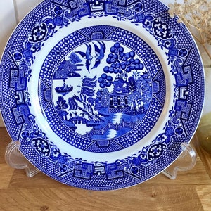 Op de afbeelding: Een blauw en wit porseleinen dinerbord met een traditioneel wilgenmotief. Het bord heeft een centraal beeld van een pagode, een wilgenboom, vogels en een boot.