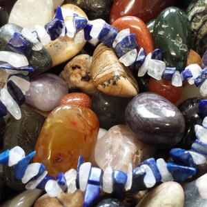 May include: A bracelet made of white and blue gemstone beads. The bracelet is laid out on a bed of various colorful stones.