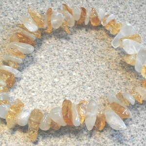 Puede incluir: Un brazalete hecho de peque&ntilde;as piezas irregulares de piedras preciosas blancas y amarillo-marr&oacute;n. El brazalete est&aacute; hecho de piedras naturales y tiene aproximadamente 18 cm de largo.