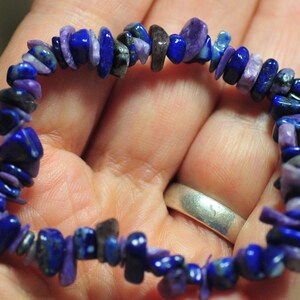 May include: A purple and blue gemstone bracelet made of small, irregular shaped chips. The bracelet is made of natural stones and is a beautiful example of handmade jewelry.