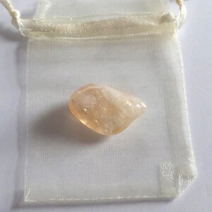 Puede incluir: Un peque&ntilde;o cristal transl&uacute;cido de color naranja claro en una bolsa de organza blanca.