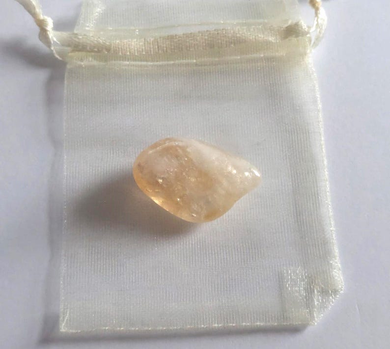 Puede incluir: Un peque&ntilde;o cristal transl&uacute;cido de color naranja claro en una bolsa de organza blanca.