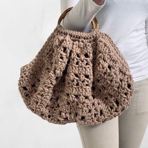 Op de afbeelding: Een grote, bruine gehaakte boodschappentas met een houten handvat. De tas heeft een textuur met open steken.