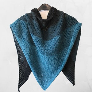 Peut inclure: Un châle triangulaire en tricot dans des tons de bleu sarcelle et noir. Le châle a une trame lâche et ouverte et est drapé sur un cintre.