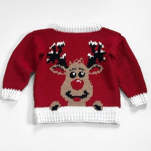 May include: A red crochet sweater featuring a reindeer design. The reindeer has brown fur, black antlers, and a smiling face. The sweater has white trim on the collar, cuffs, and bottom hem, perfect for the holiday season.