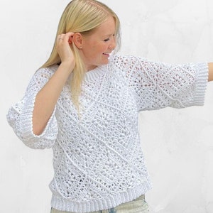 Op de afbeelding: Een witte gehaakte trui met een losse pasvorm en een delicaat opengewerkt patroon. De trui heeft een ronde hals en driekwart mouwen.