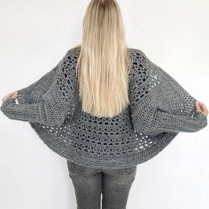 May include: A gray crochet cardigan with a loose, open-weave design. The cardigan is shown from the back, with the sleeves pulled back to show the open weave.