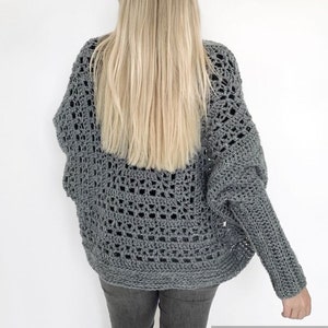 May include: A gray crochet cardigan with a lacy pattern. The cardigan has long sleeves and a loose fit.