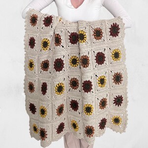 Op de afbeelding: Een gehaakt deken met een zonnebloemmotief in tinten bruin, geel en crème.