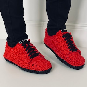 Op de afbeelding: Rode gehaakte sneakers met zwarte veters. De sneakers hebben een zwarte rubberen zool.