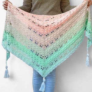 May include: A triangular crochet shawl featuring a gradient color pattern that transitions from soft peach at the top to light green and pale blue at the bottom. The shawl has an intricate openwork butterfly motif and three light blue tassels.