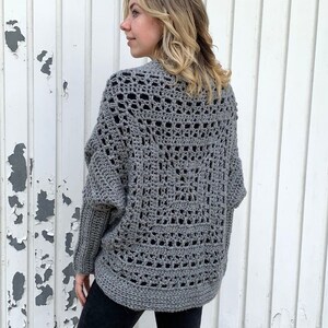 May include: A gray crochet cardigan with a lacy pattern. The cardigan has long sleeves and a loose fit.