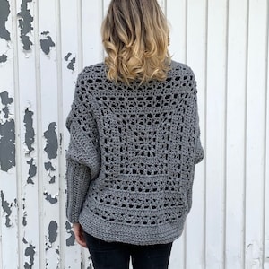May include: Gray crochet cardigan with a lacy openwork design. The cardigan has a relaxed fit and long sleeves.