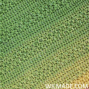 May include: Close-up of a green, yellow and orange crochet fabric with a sparkly thread. The fabric has a diagonal pattern.