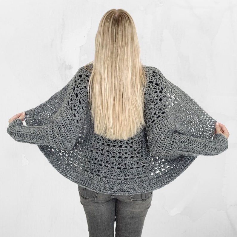 May include: A gray crocheted cardigan with a loose, open-weave design. The cardigan has a wide, rounded neckline and long sleeves.