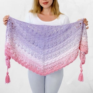 May include: A crocheted shawl with a gradient of pink, white, and purple. The shawl has a delicate lace pattern and two tassels.