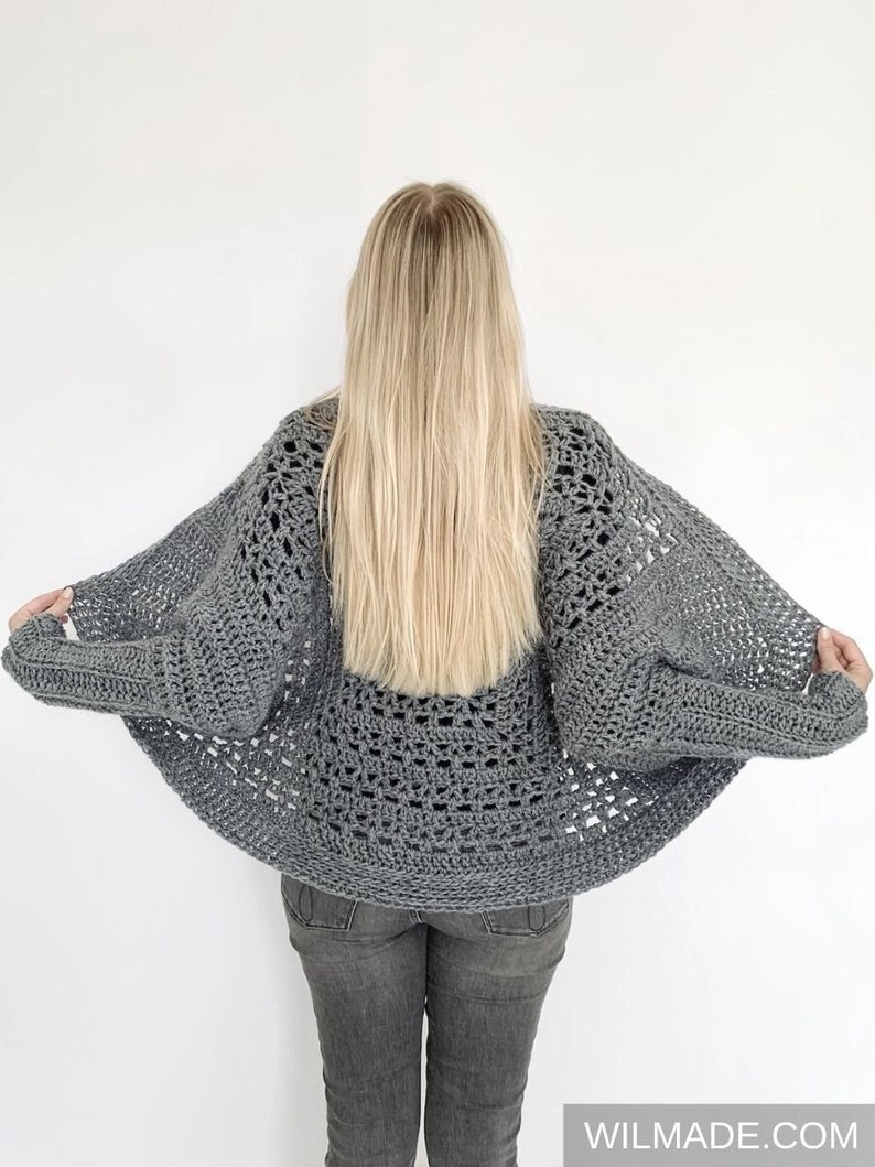 May include: A gray crochet cardigan with a loose, open-weave design. The cardigan is shown from the back, with the sleeves pulled back to show the open weave.