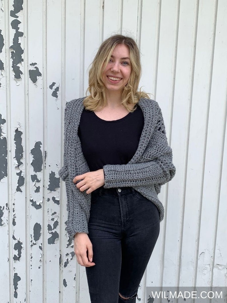 May include: A gray crocheted cardigan with a loose fit and open front. The cardigan has a textured stitch pattern and long sleeves.