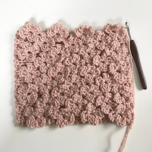Op de afbeelding: Een close-up van een roze gehaakt deken met een bloemenpatroon. Het deken is gemaakt met een vaste steek en heeft een textuur.