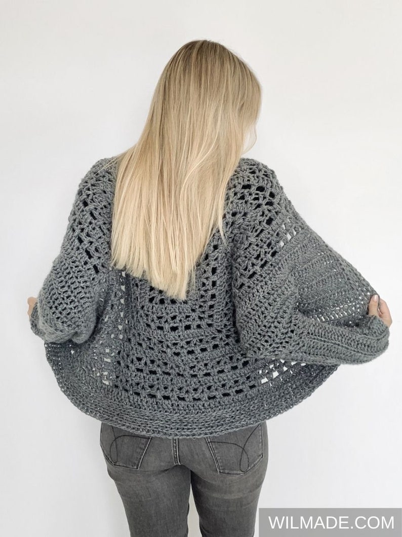 May include: A gray crochet cardigan with a lacy openwork design. The cardigan is shown from the back and has a relaxed fit.