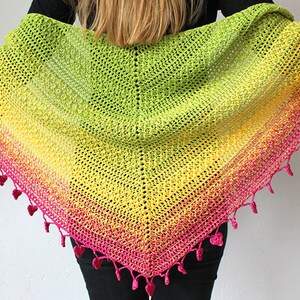 May include: A colourful crochet shawl with a gradient of pink, yellow and green. The shawl has a fringe of pink yarn with small heart-shaped pom-poms.