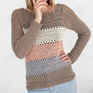 Op de afbeelding: Een gebreide trui met lange mouwen in de kleuren bruin, crème, perzik en grijs.