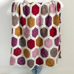 Op de afbeelding: Een gehaakt deken met een honingraatpatroon in tinten rood, roze, paars, bruin en goud.