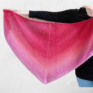 Op de afbeelding: Een roze en witte ombre gehaakte sjaal met een delicaat steekpatroon.