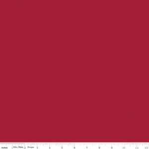 May include: A solid deep red fabric swatch featuring a smooth, uniform texture. At the bottom edge, a white ruler is visible, displaying measurements in inches from 1 to 12, with the text Riley Blake Designs printed near the 1-inch mark.