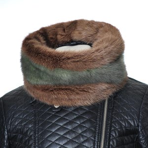 Könnte beinhalten: Ein luxuriöser Fell-Halswärmer in Braun- und Grüntönen. Der Halswärmer hat in der Mitte ein Band aus grünem Fell. Er wird über einer schwarzen, gesteppten Lederjacke getragen.