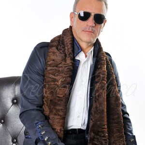 May include: A man wearing a dark blue jacket with gold buttons and a brown fur scarf. He is also wearing sunglasses and a white shirt. The background is white.