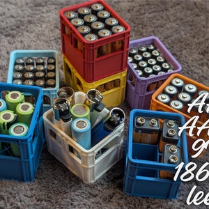 Könnte beinhalten: Eine Sammlung leerer Batteriekisten in verschiedenen Farben, darunter Blau, Rot, Lila, Gelb und Orange. Die Kisten sind gefüllt mit AA-, AAA-, 9V- und 18650-Batterien. Der Text "AA AAA 9V 18650 leer" ist im Bild sichtbar.