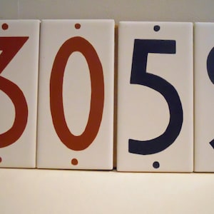May include: Four white ceramic tiles with black and brown numbers. The numbers are 3059.